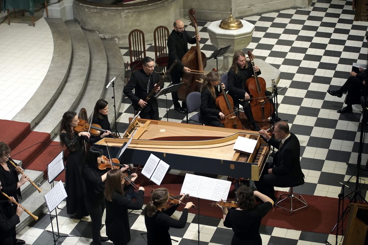 grupa muzyków grająca na instrumentach smyczkowych stoi przy fortepianie