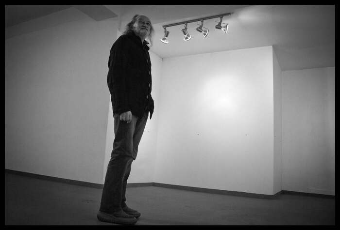 mężczyzna stojący w pustej sali ekspozycyjnej, pod sufitem reflektory, zdjęcie czarno białe