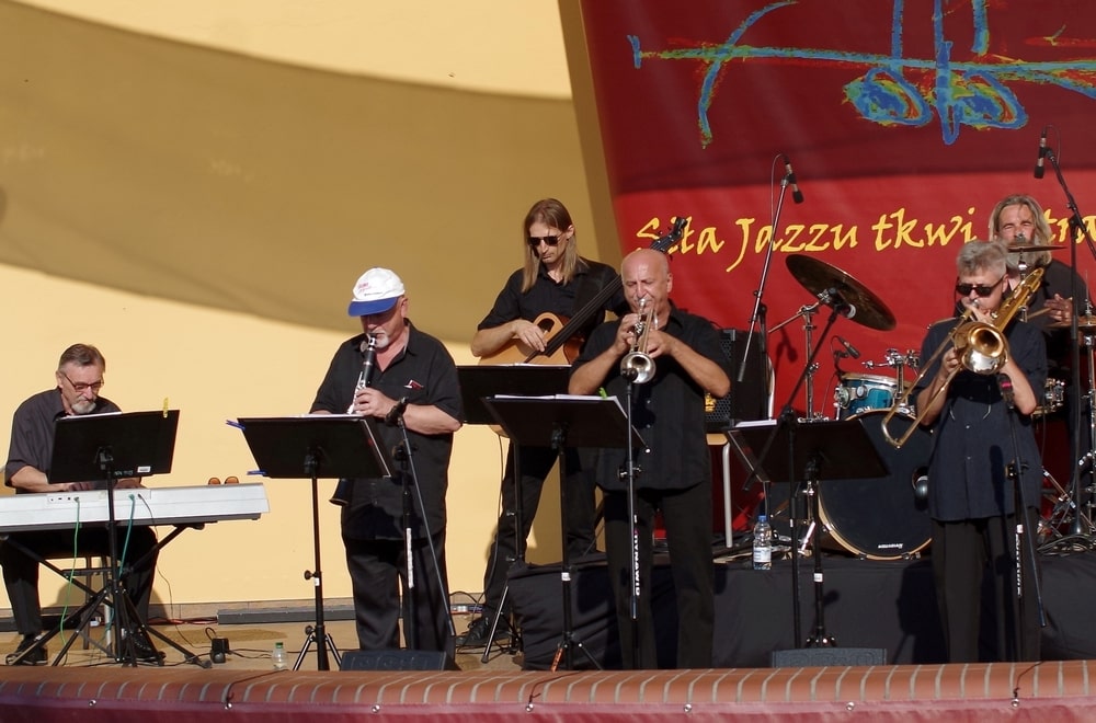 fotografia: grupa muzyków z instrumentami na scenie plenerowej, grają oświetleni słońcem. Projekt Swing Club na Mazowszu.