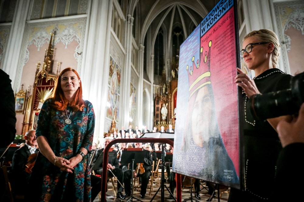 Małgorzata Kalicińska stoi we wnętrzu kościoła, obok stoi Ewa Krzysik i trzyma portret Małgorzaty Kalicińskiej