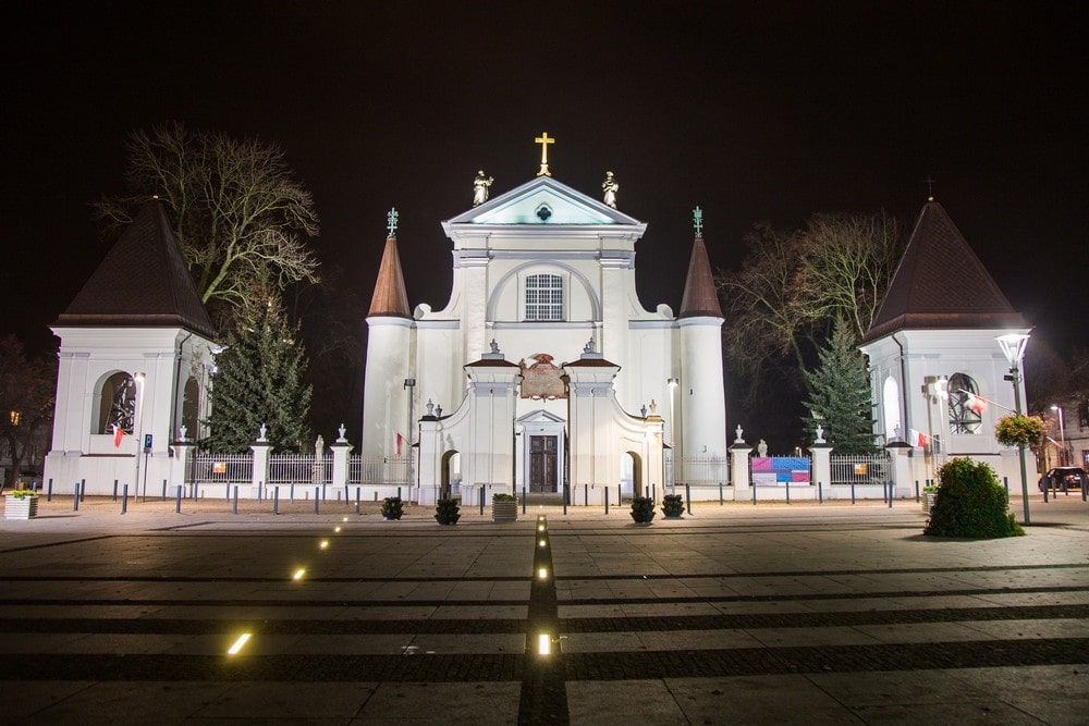 fotografia: biały front bazyliki w Węgrowie, sfotografowany nocą, podświetlony