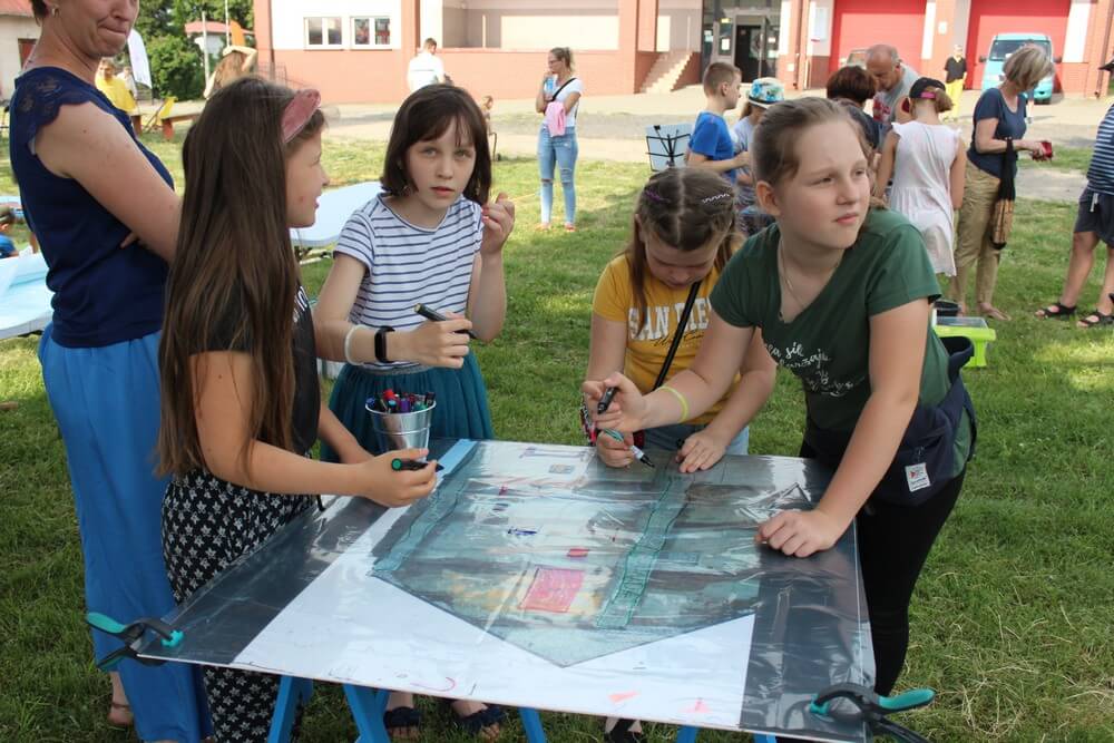 fotografia: cztery dziewczynki malują na planszy rozłożonej na stole Karawana Wędrujący Festiwal Sztuki i Animacji