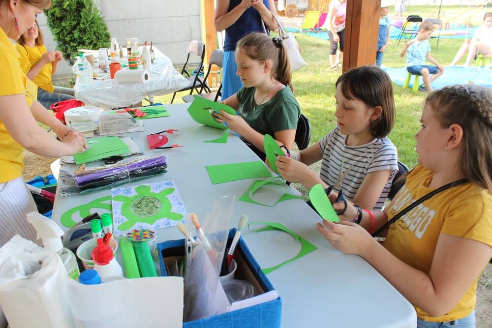 fotografia: trzy dziewczynki siedzą przy stoliku i wycinają kolorowy papier Karawana Wędrujący Festiwal Sztuki i Animacji