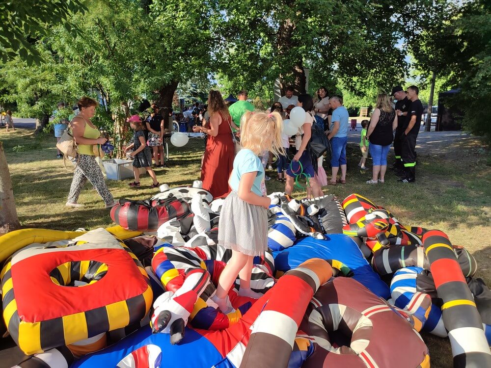 fotografia: dziewczynka stoi na stercie kolorowych poduszek, leżących na trawie w parku Karawana Wędrujący Festiwal Sztuki i Animacji