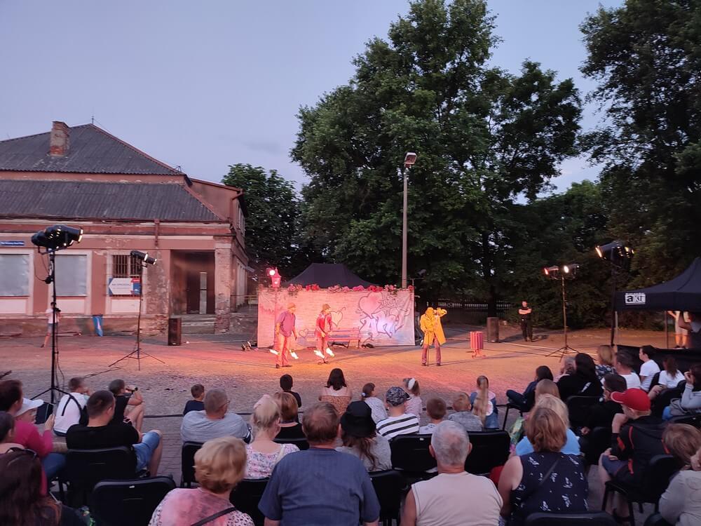 fotografia: publiczność oglądająca spektaklu teatru akt na placu, w tle budynek. Karawana Wędrujący Festiwal Sztuki i Animacji