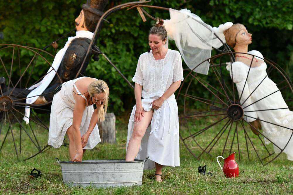 fotografia: scena ze spektaklu, dwie kobiety stoją przy metalowej misie i myją nogi