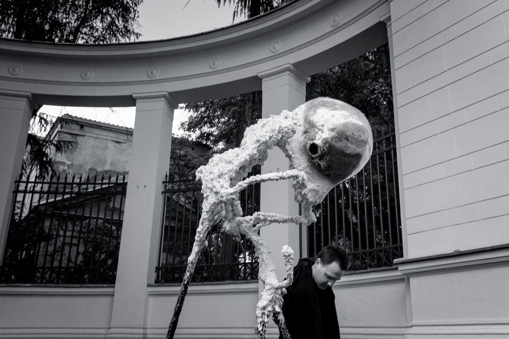 fotografia: na tle kolumnady rzeźba abstrakcyjna, obok autor Jan Gostyński