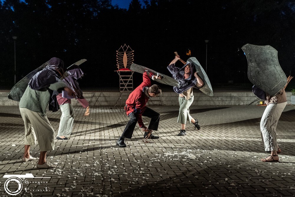 fotografia: scena ze spektaklu plenerowego, grupa ludzi walczących na białą broń