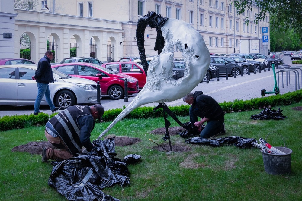 fotografia: montaż rzeźby abstrakcyjnej na trawniku przed budynkiem MIK, dwie osoby pracują przy montażu