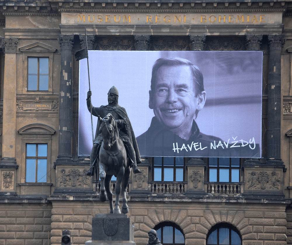 fotografia: baner z portretem Vaclava Havla zawieszony na budynku, na pierwszym planie rzeźba zbrojnego mężczyzny na koniu