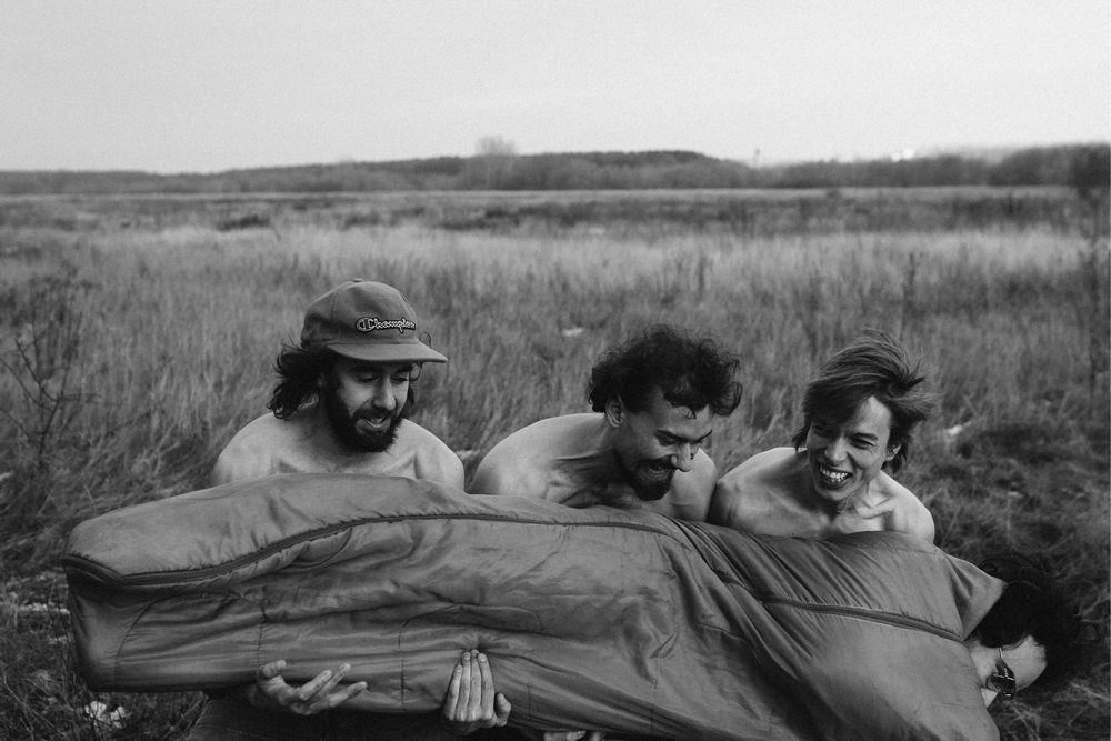 fotografia czarno biała: trzech mężczyzn trzyma czwartego zawiniętego w śpiwór