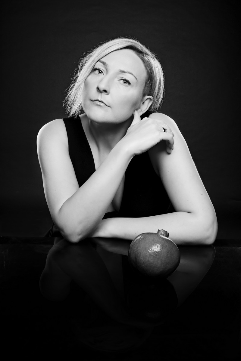 fotografia czarno biała: portret anny gadt, opiera się o blat, przed nią okrągły owoc
