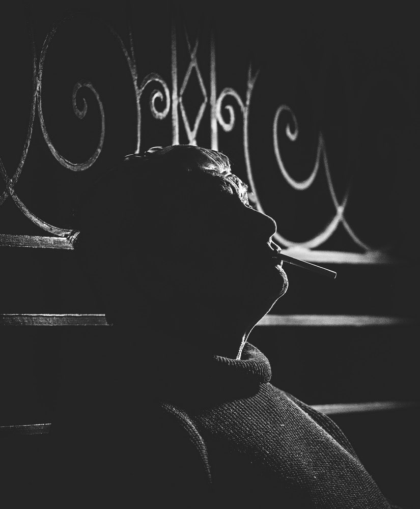fotografia czarno biała: marcin świetlicki, ciemne tło, podświetlony zarys głowy, w ustach trzyma papierosa