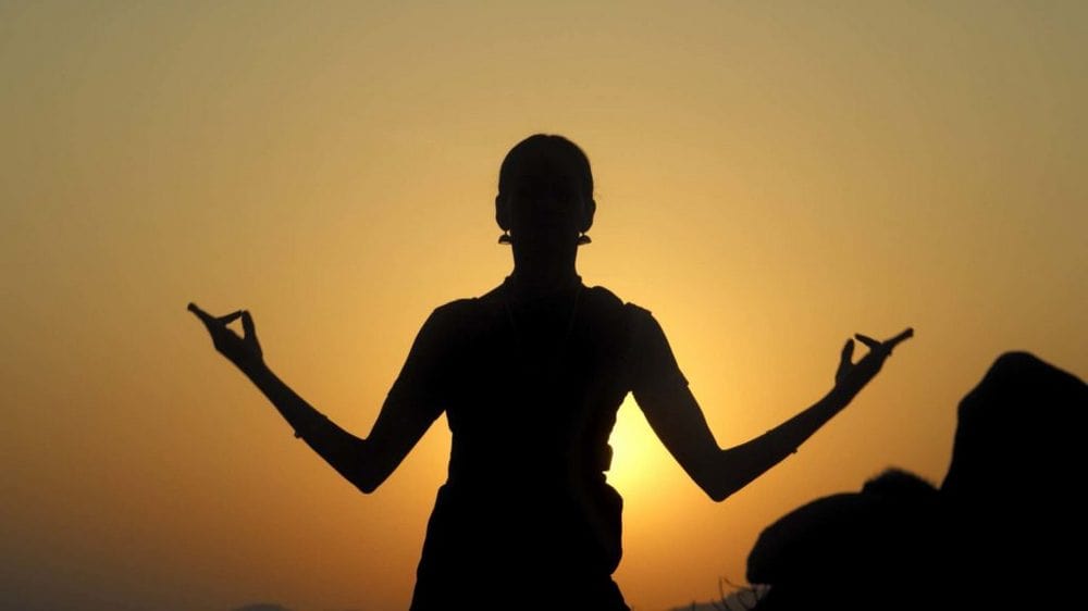 fotografia: sylwetka kobiety z uniesionymi ramionami na tle rozświetlonym światłem słonecznym