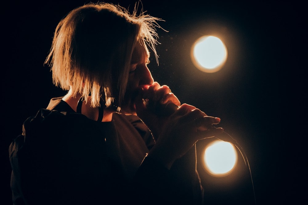 fotografia: anna gadt śpiewa z mikrofonem przy ustach, zbliżenie prawego profilu, podświetlona reflektorem