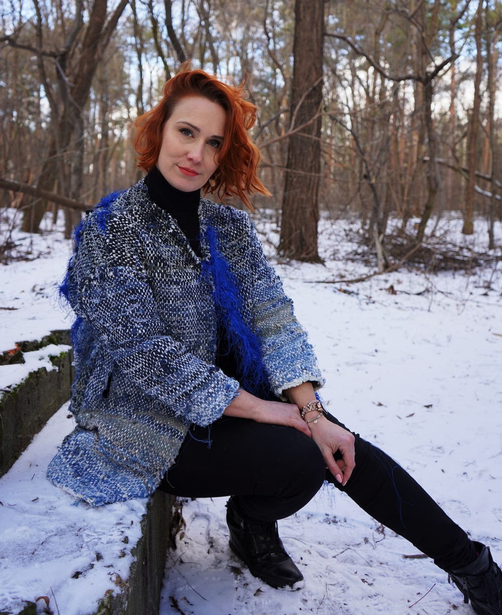 fotografia: anna hlebowicz siedzi na kamiennym schodku, ubrana w niebieski płaszcz swojego autorstwa, w tle zaśnieżony las
