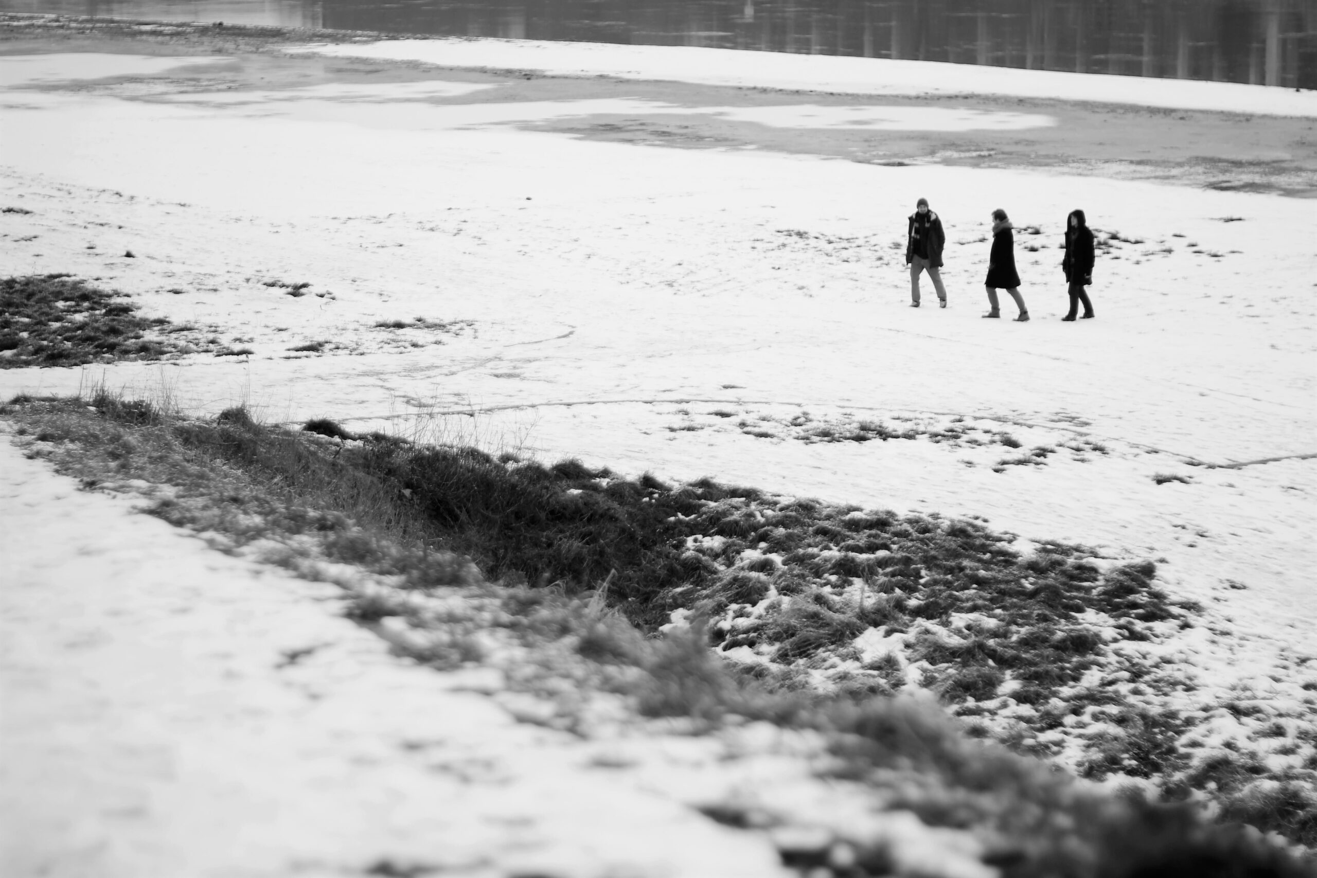 fotografia czarno biała: trzech mężczyzn widzianych z oddali, idzie po śniegu