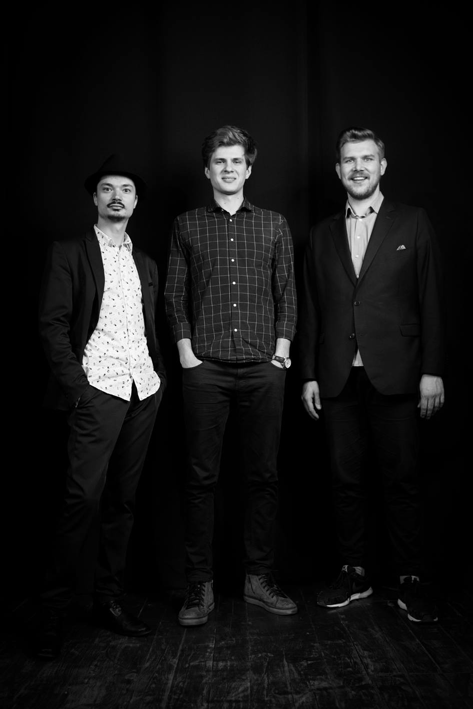 fotografia czarno biała: trzech młodych mężczyzn stoi obok siebie, na ciemnym tle