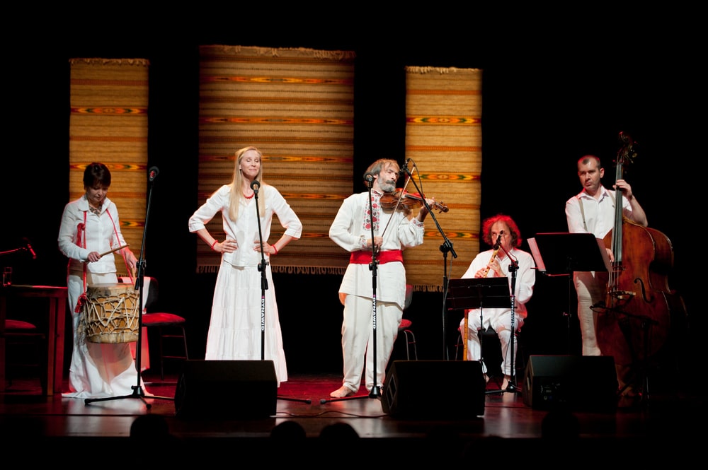 fotografia: pięcioro muzyków i wokalistów na scenie, z instrumentami, ubrani w stroje w stylistyce ludowej
