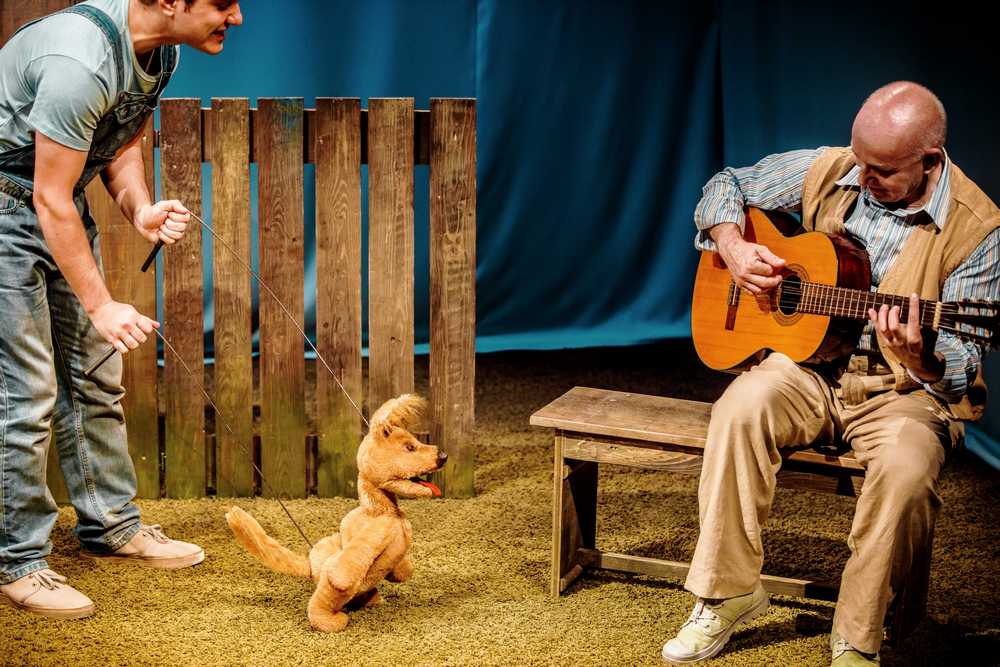 fotografia: zdjęcie ze spektaklu, dwóch mężczyzn - jeden z gitarą, drugi trzyma w rękach druty, którymi animują pacynkę psa