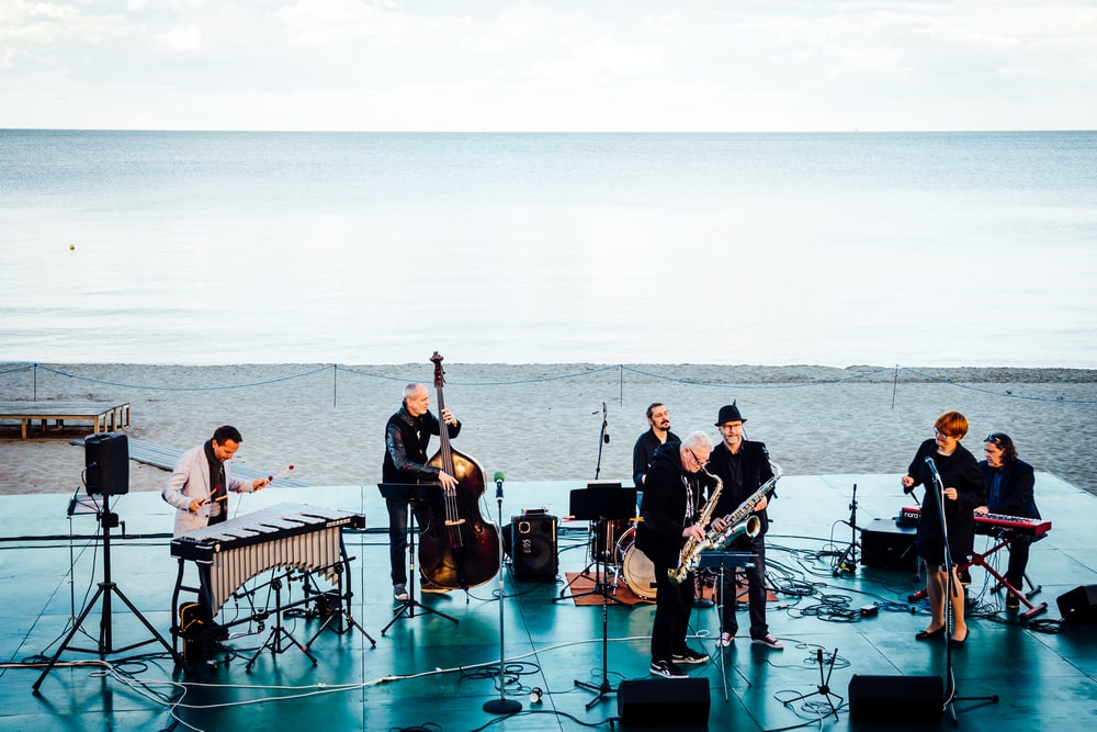 fotografia: grupa muzyków grających na scenie umiejscowionej na plaży, w tle morze