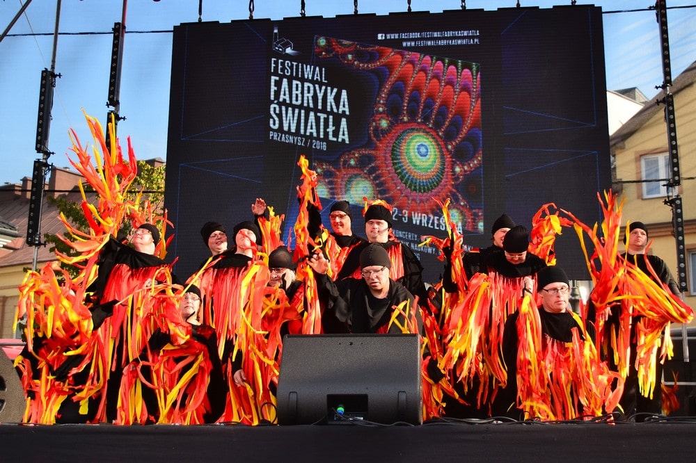 fotografia tancerze balonika na scenie, do czarnych strojów mają przyczepione czerwono żółte wstęgi