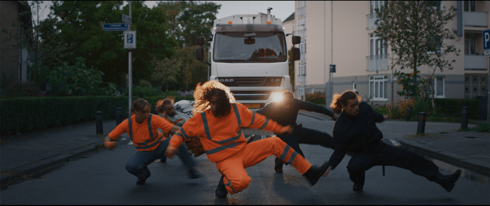 fotografia pięciu mężczyzn tańczących synchronicznie na ulicy, za nimi samochód ciężarowy