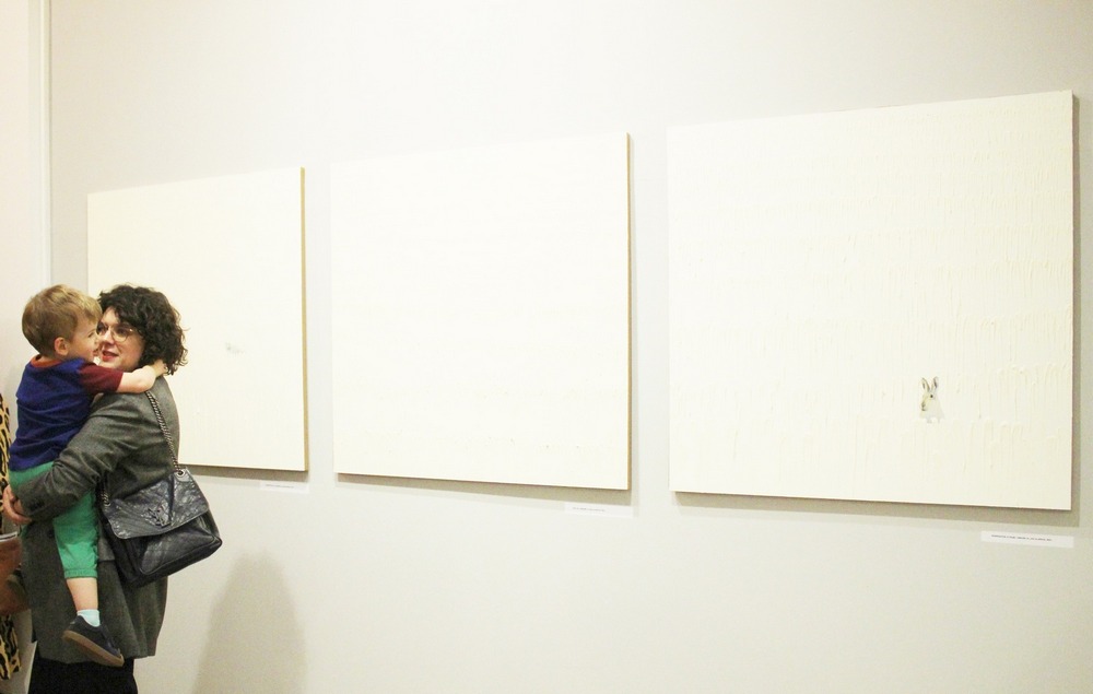 fotografia - trzy białe obrazy na ścianie, obok nich kobieta z dzieckiem na ręku