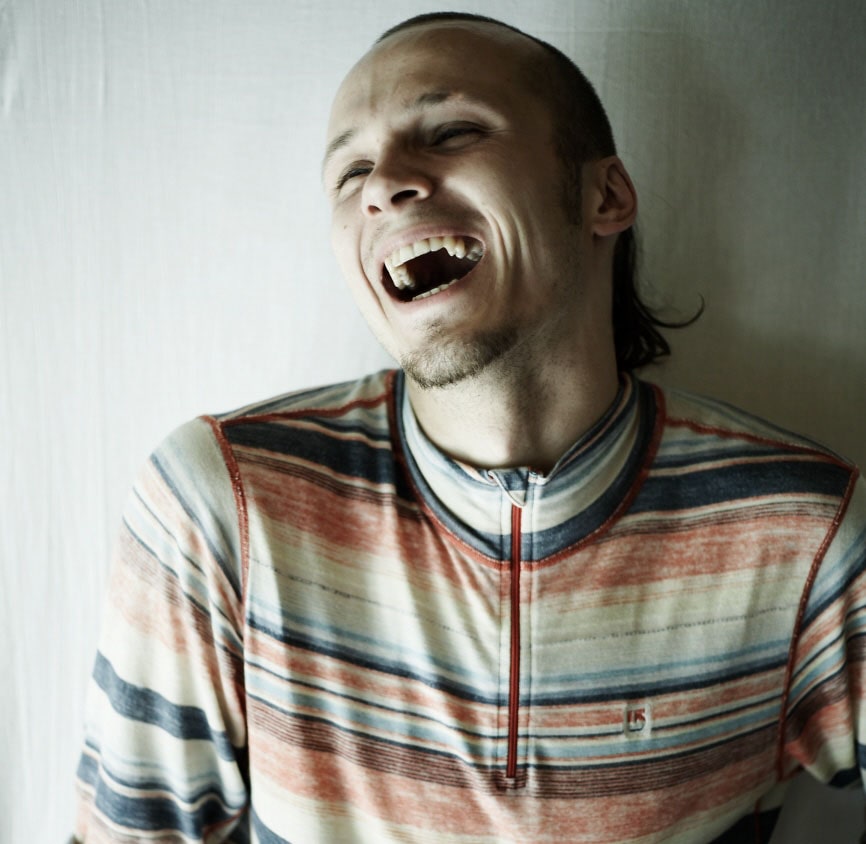 fotografia - Sebastian Flegiel w szerokim uśmiechu w pasiastej bluzie, zdjęcie portretowe