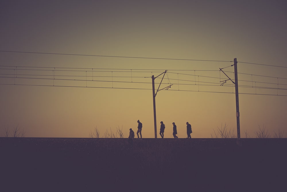 fotografia - pięć sylwetek ludzi idących szczytem nasypu kolejowego