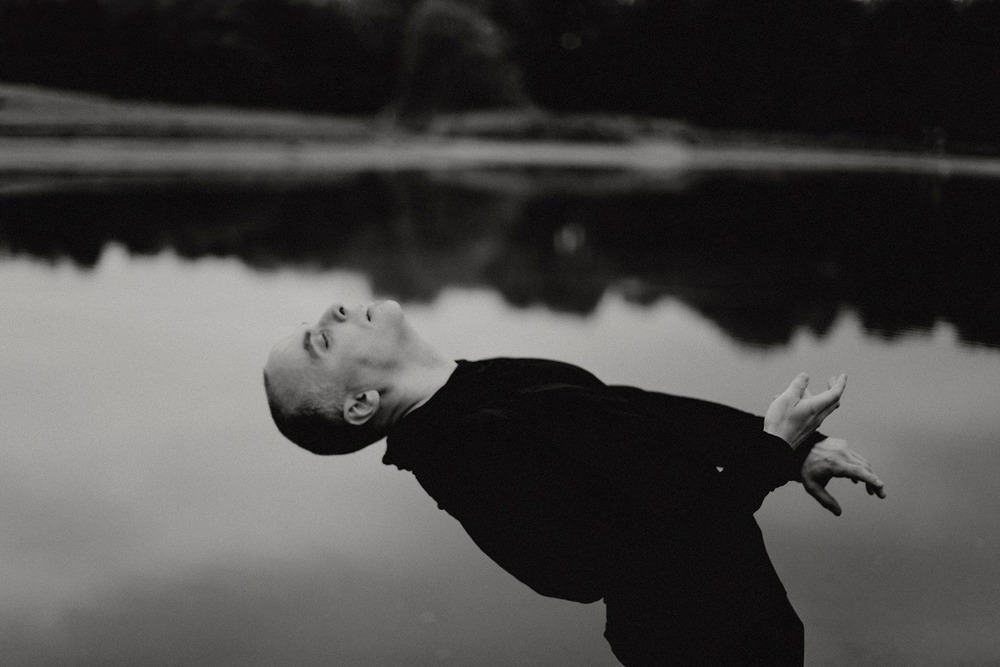 fotografia czarno biała Filip Wencki odchylony do tyłu, poza balansem - na tle jeziora