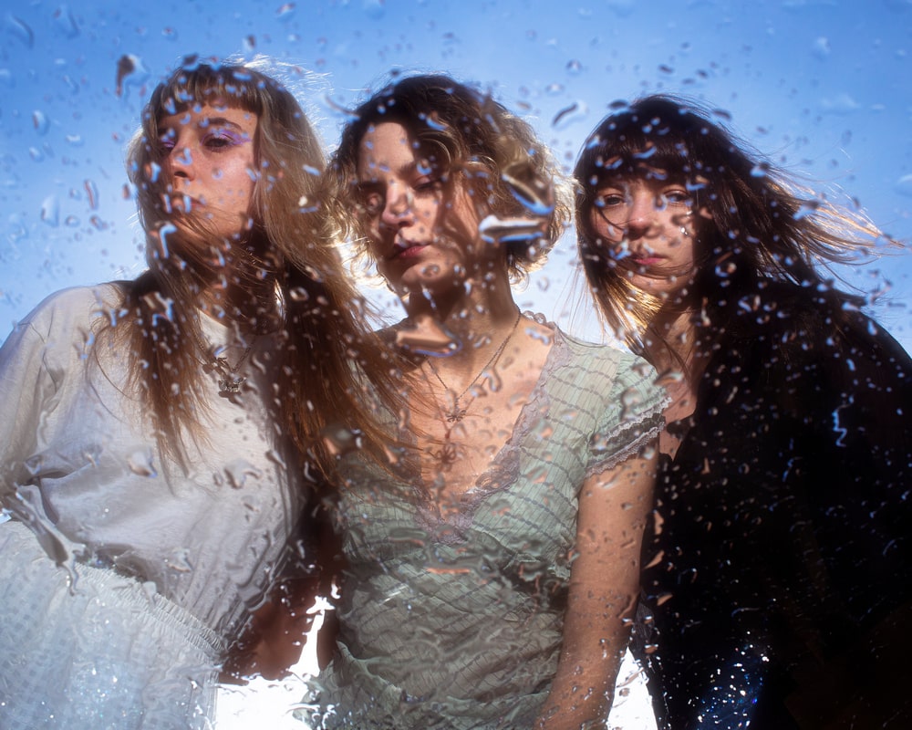 fotografia trzy kobiety sfotografowane przez szybę na której są krople wody w tle błękit niega