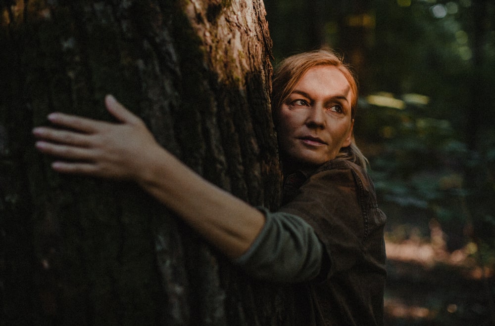 fotografia kobiety obejmującej pień drzewa