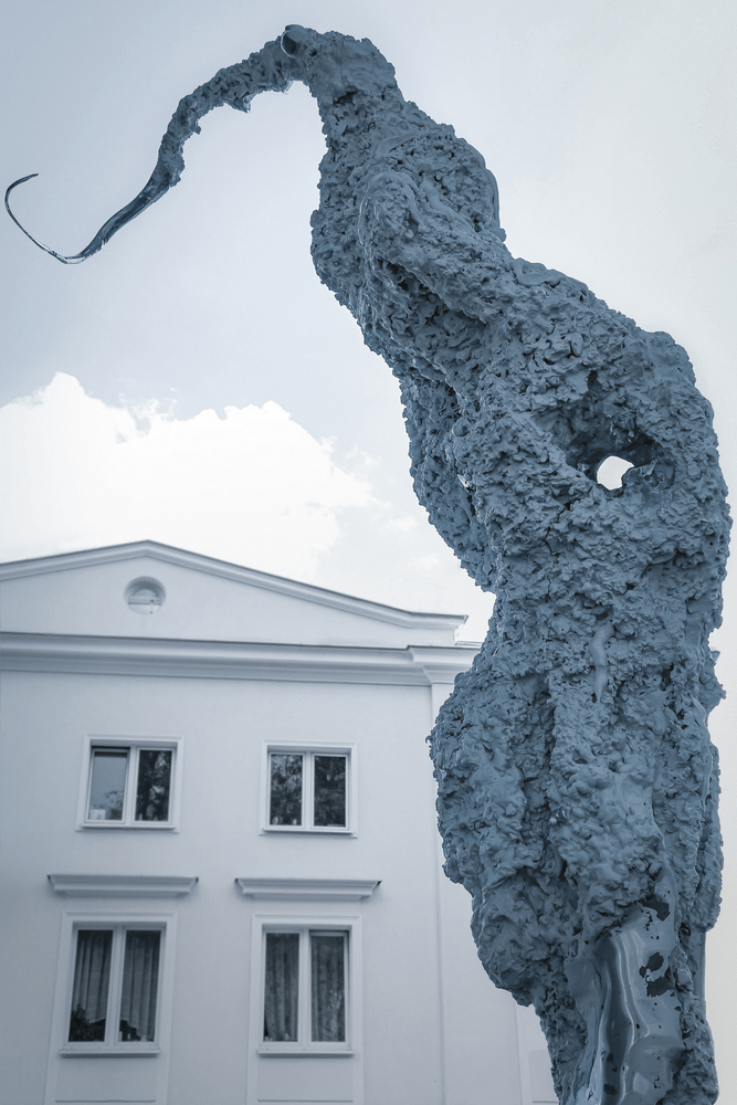 fotografia fragment rzeźby abstrakcyjnej na tle białego budynku i nieba