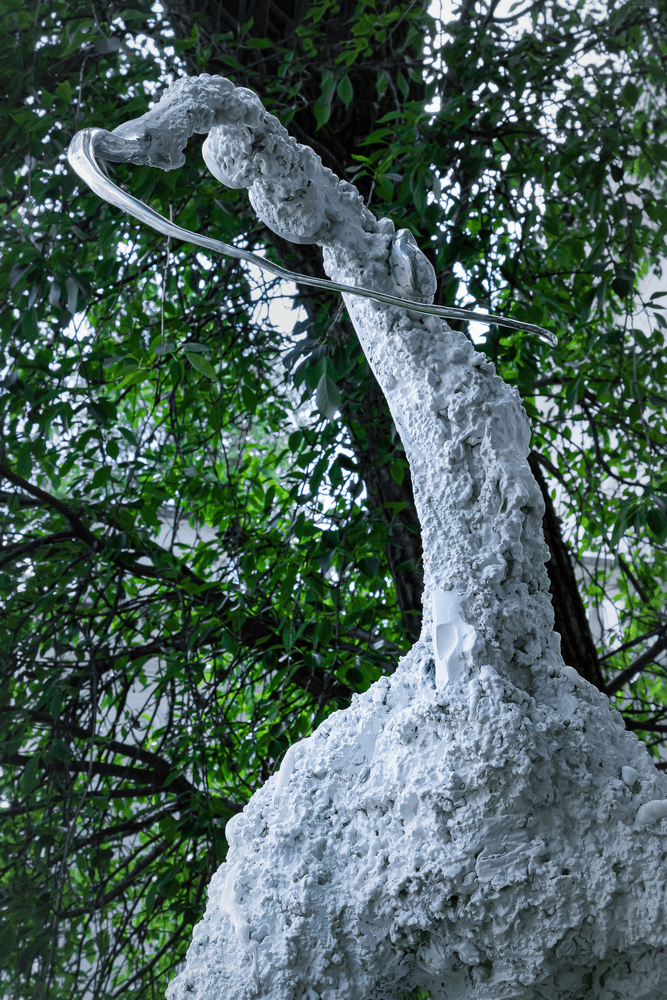 fotografia fragment rzeźby abstrakcyjnej na tle zielonych liści drzewa