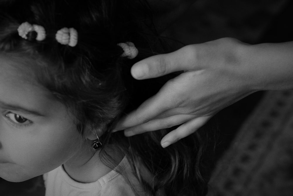 fotografia czarno biała fragment twarzy młodej kobiety, widoczna dłoń dotykająca z tyłu jej głowy