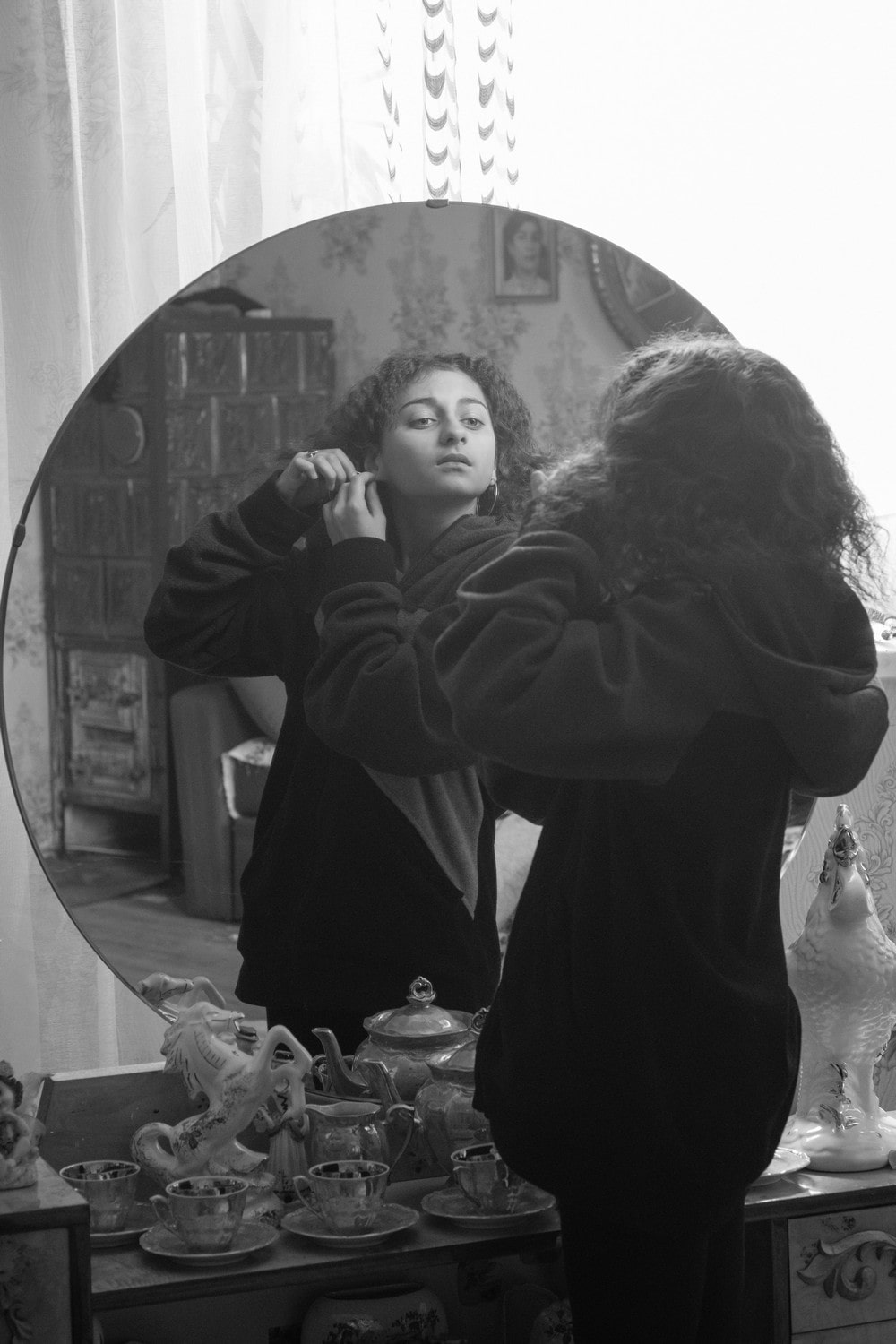 fotografia czarno biała młoda kobieta stoi przed lustrem i zakłada kolczyki do ucha