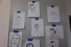 fotografia - tablica z przypiętymi rysunkami twarzy wykonanymi przez dzieci