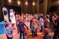 fotografia - kilkudziesięcio osobowa grupa dzieci na sali teatralnej, stoją przed aktorem