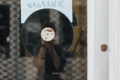 fotografia: zbliżenie na szklane drzwi na których wisi płyta winylowa i napis trwa nagranie